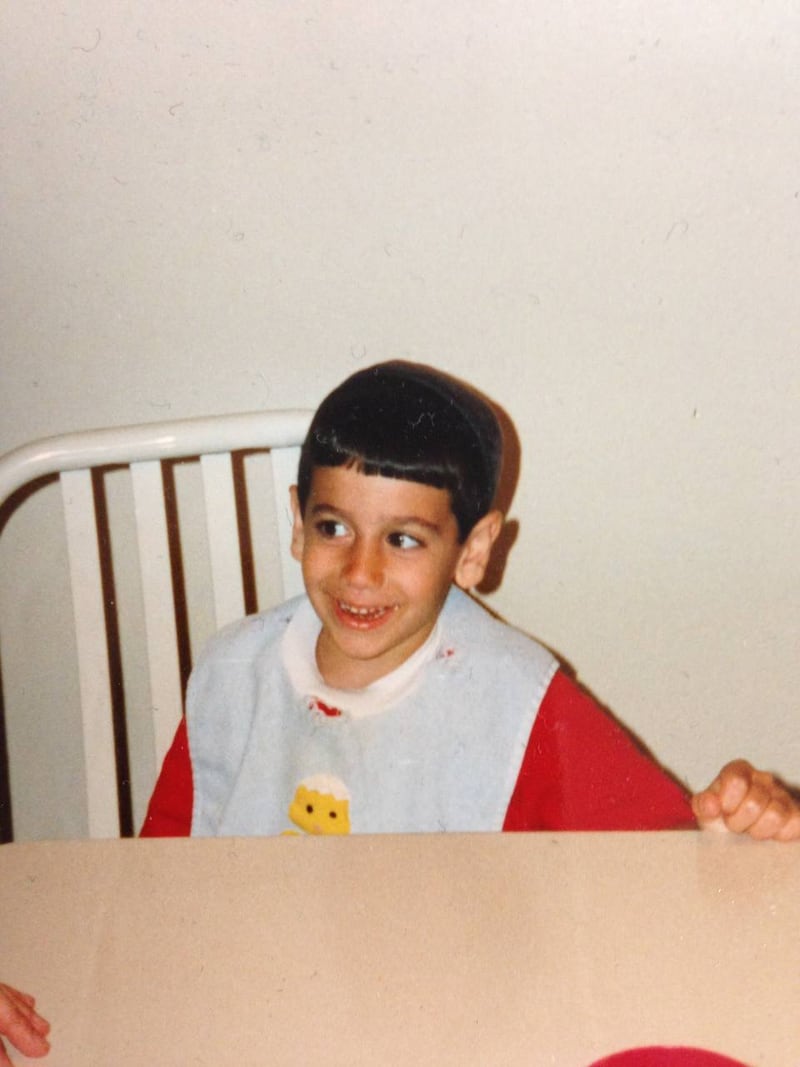 Joe as a young Orthodox boy in Chicago, seated in a high chair with a bowl cut, grinning.